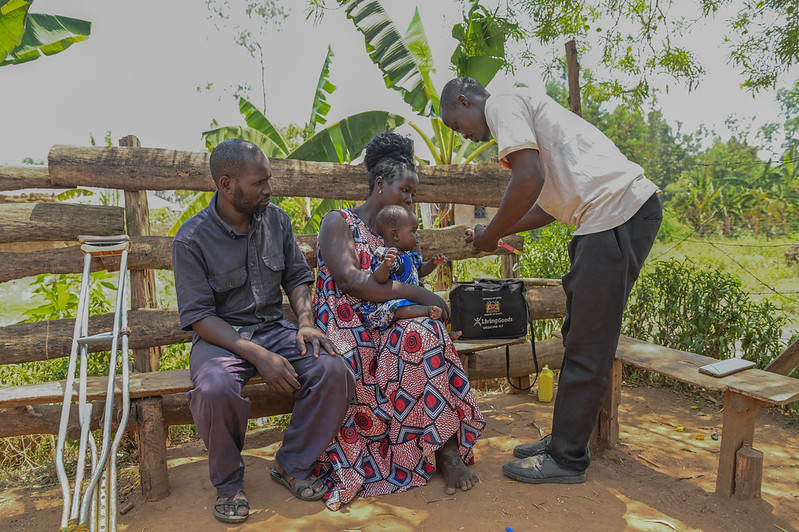 Community Health Promoter David Okumu preparing to examine Zahara Khavere in the arms of her mother (Client). Komiriai, Busia.